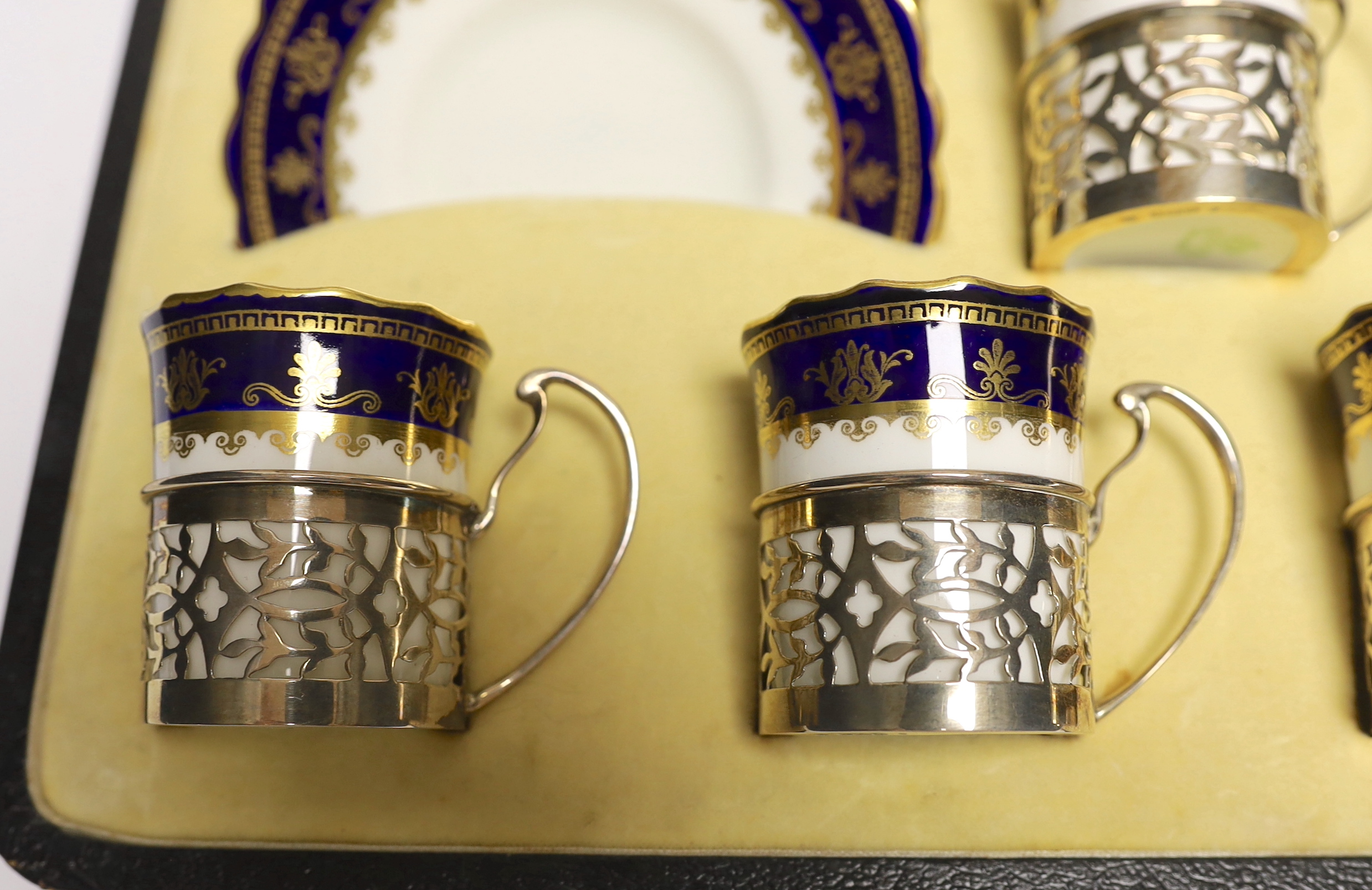 A cased George V set of six Aynsley coffee cans and saucers, the cans with pierced silver holders, C.S. Green & Co, Birmingham, 1924, can 57mm.